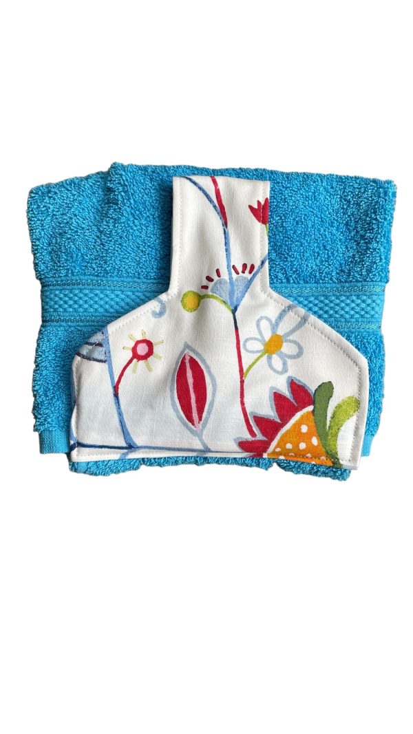 Hand towel to hang on kitchen or Aga rail. Fastened with a magnetic popper. Towel turquoise blue. Top off white with multicloured abstract flower design.